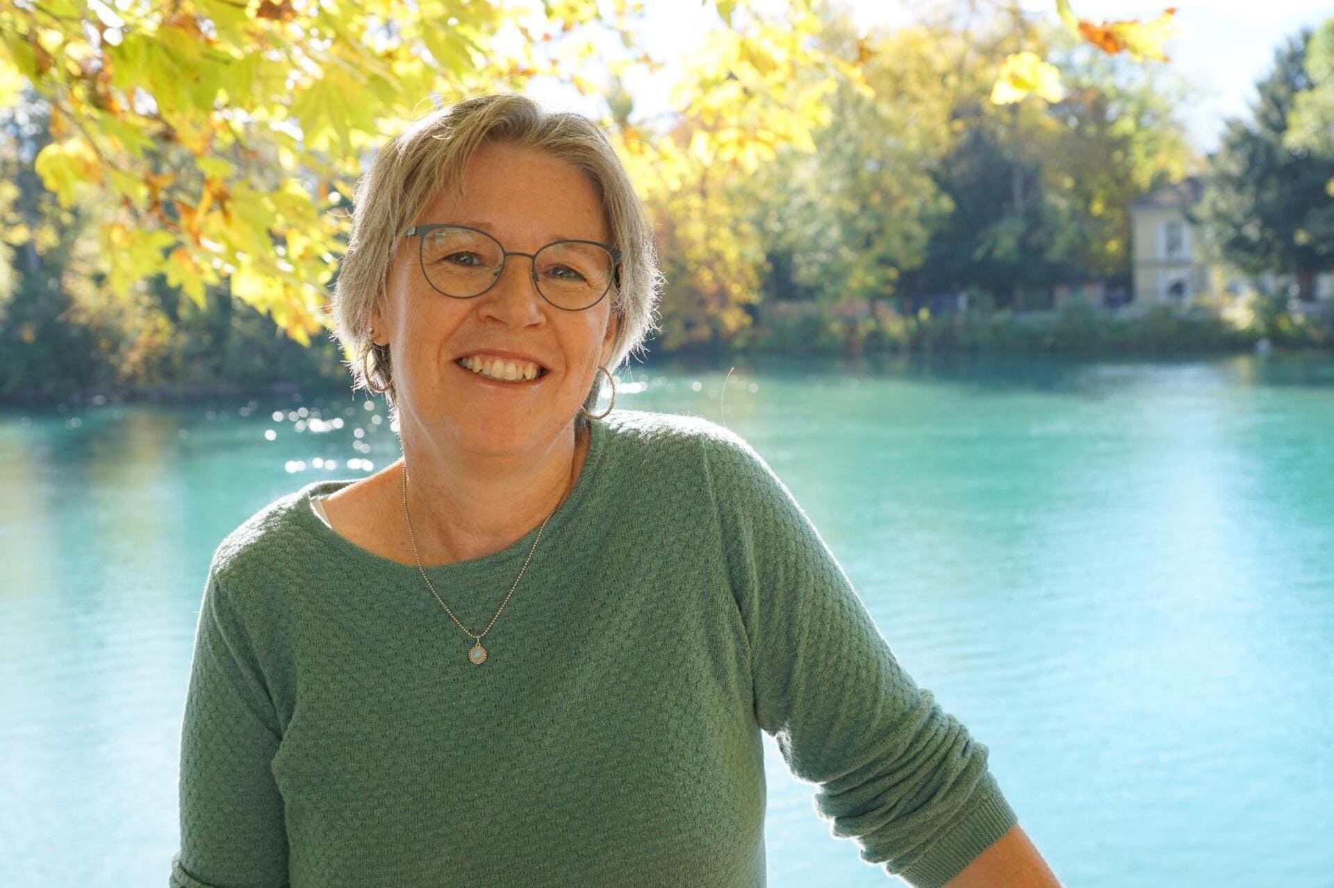 Mitglied vom FrauenRaum Netzwerk Claudia Scheidegger lächelt in die Kamera, hinter ihr ist der Thunersee unscharf zu erkennen.