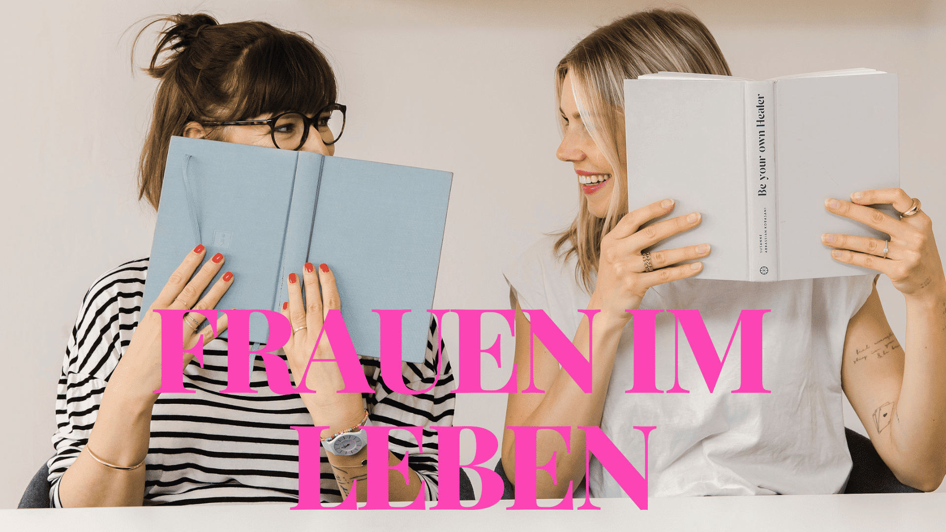Die 2 Gründerinnen vom Podcast Frauen im Leben vom FrauenRaum Verein lächeln sich gegenseitig an und halten jeweils ein Buch vor das Gesicht.