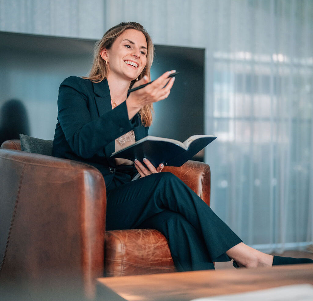 Mitglied vom FrauenRaum Netzwerk Nathalie Hauenstein sitzt in einem Sessel und hält ein Buch und Stift in der Hand.