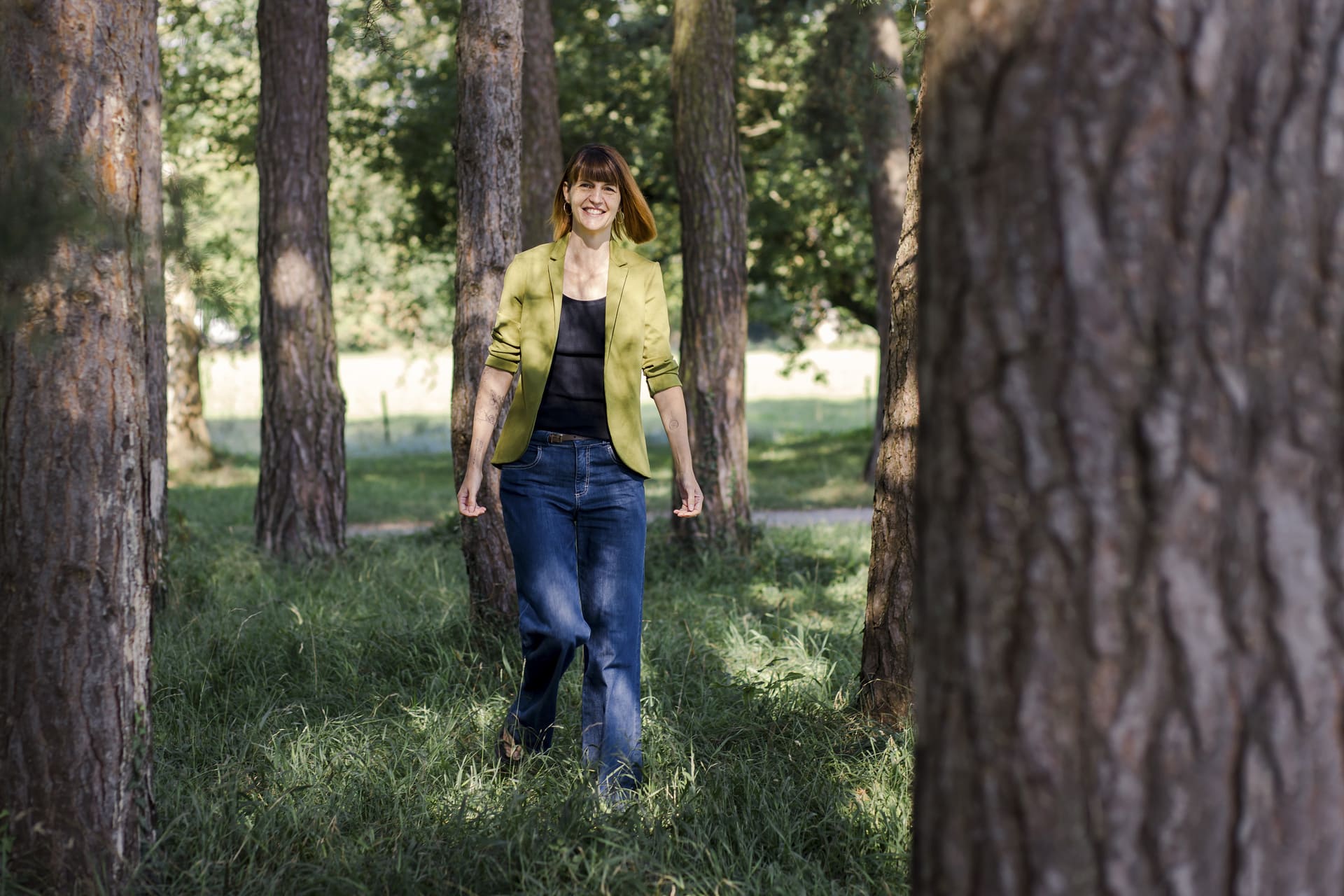 Petra Gerber Photographie ein Mitglied vom FrauenRaum Netzwerk steht im Wald und lächelt in die Kamera.